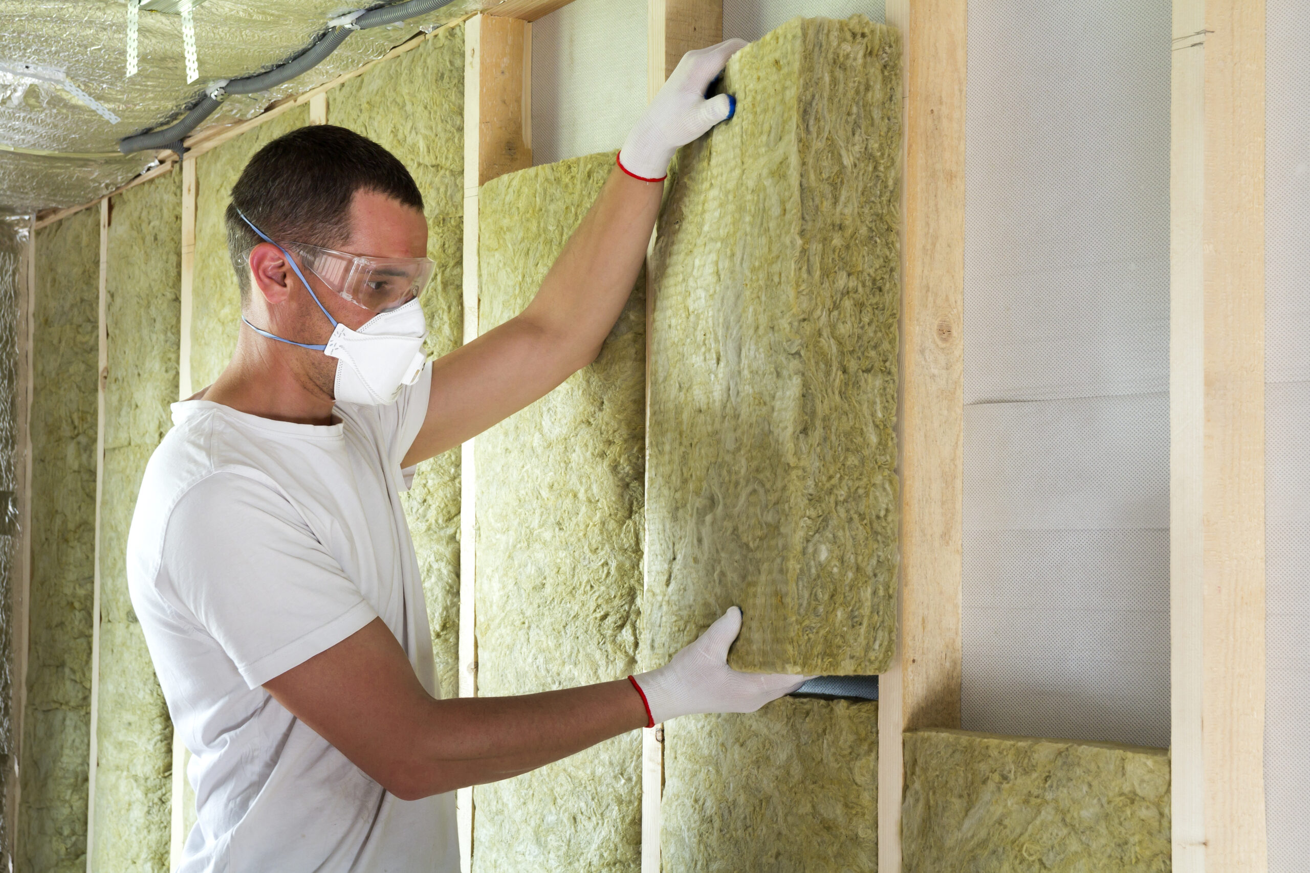 Worker in protective goggles and respirator insulating rock wool